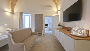 Ein modernes Hotelzimmer mit einer Couch, einem Flachbildfernseher, einer Holztresen und einer dekorativen Leuchte.