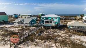 A beachfront property with multiple buildings, including a prominent turquoise house with a balcony and a pool, connected by wooden walkways. - Luxurious Gulf-front Home W/ Private Pool - 5 Br 5.5 Ba (Gulf Shores)