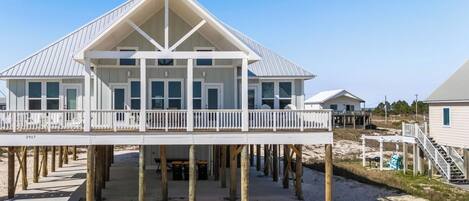 A beachfront house with a balcony, wooden deck, and a clear view of the ocean.
