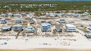 Ett flygbildsfoto av ett bostadsområde vid kusten med flera hus som ligger direkt vid stranden, en sandstrand och en skog i bakgrunden.