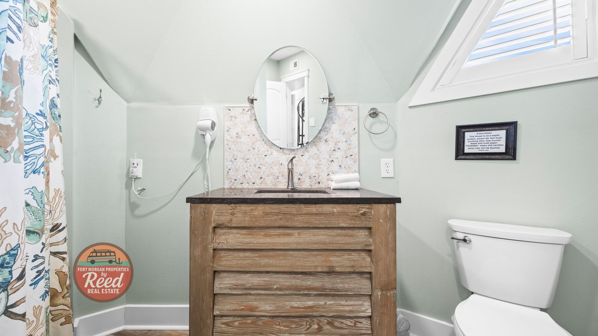 Une salle de bain avec un meuble-lavabo en bois, des toilettes blanches, un miroir et un rideau de douche orné d’un motif de feuilles.