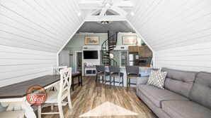 Ett kompakt bostadsutrymme med matplats, soffa, kök och en trappa.