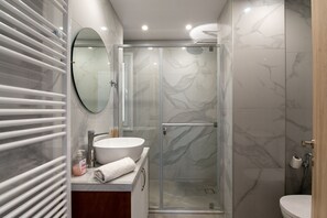 A modern bathroom with a glass-enclosed shower, a round mirror, and a white sink. - Stella s House Near the Sea in Tavronitis (Platanias)
