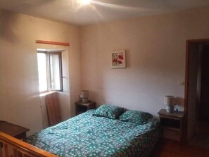 A bedroom with a bed, a window, a nightstand, and a wall-mounted lamp. - Mas du Roy (Sénéchas)
