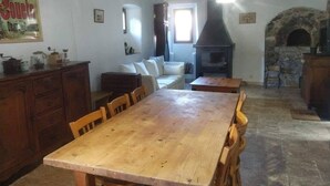 A rustic interior with a wooden dining table, stone fireplace, and stone walls. - Mas du Roy (Sénéchas)