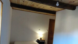 A small, narrow room with a single bed, a nightstand with a lamp, and a wooden door. - Mas du Roy (Sénéchas)