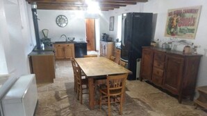A kitchen with a dining table, chairs, a refrigerator, cabinets, a clock, and a poster on the wall. - Mas du Roy (Sénéchas)