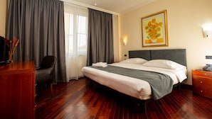 A hotel room with a large bed, a desk, a chair, a nightstand, and a painting on the wall. - Pushkin Hotel (Uralsk)