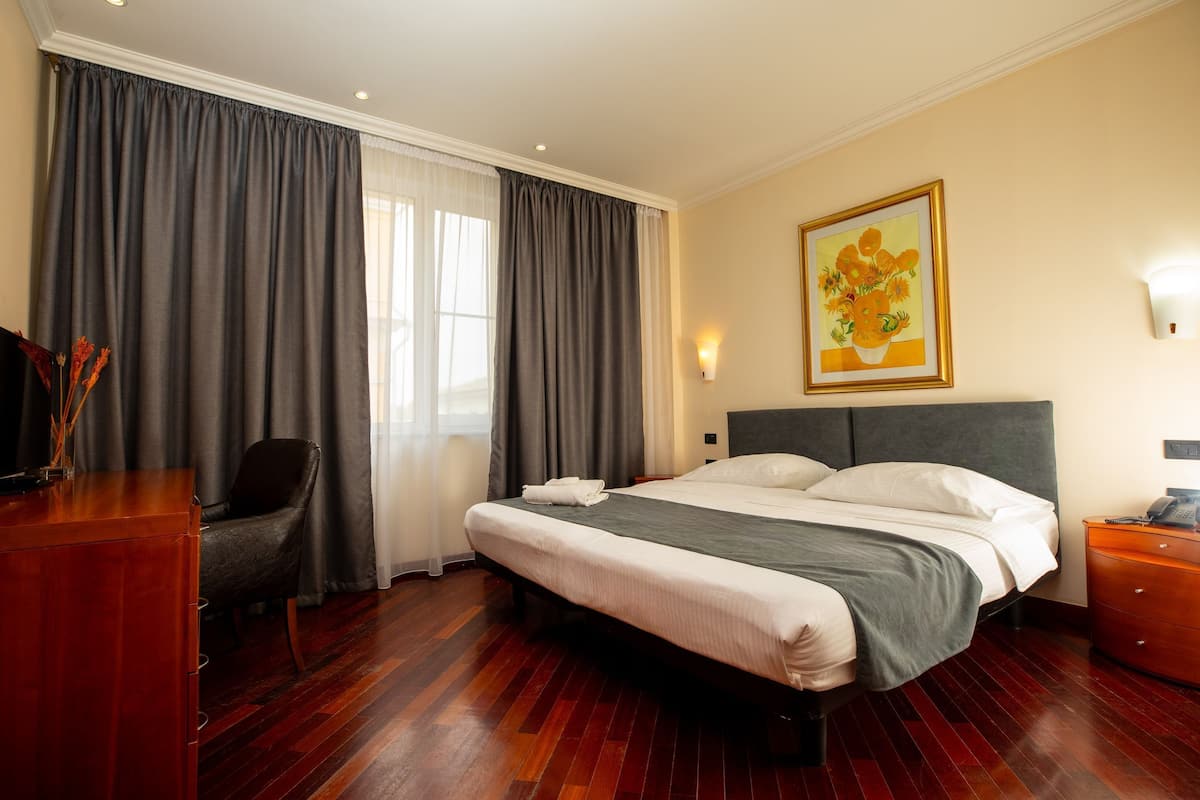 Ein Hotelzimmer mit einem großen Bett, einem Schreibtisch, einem Sessel, einem Nachttisch und einem Bild an der Wand.
