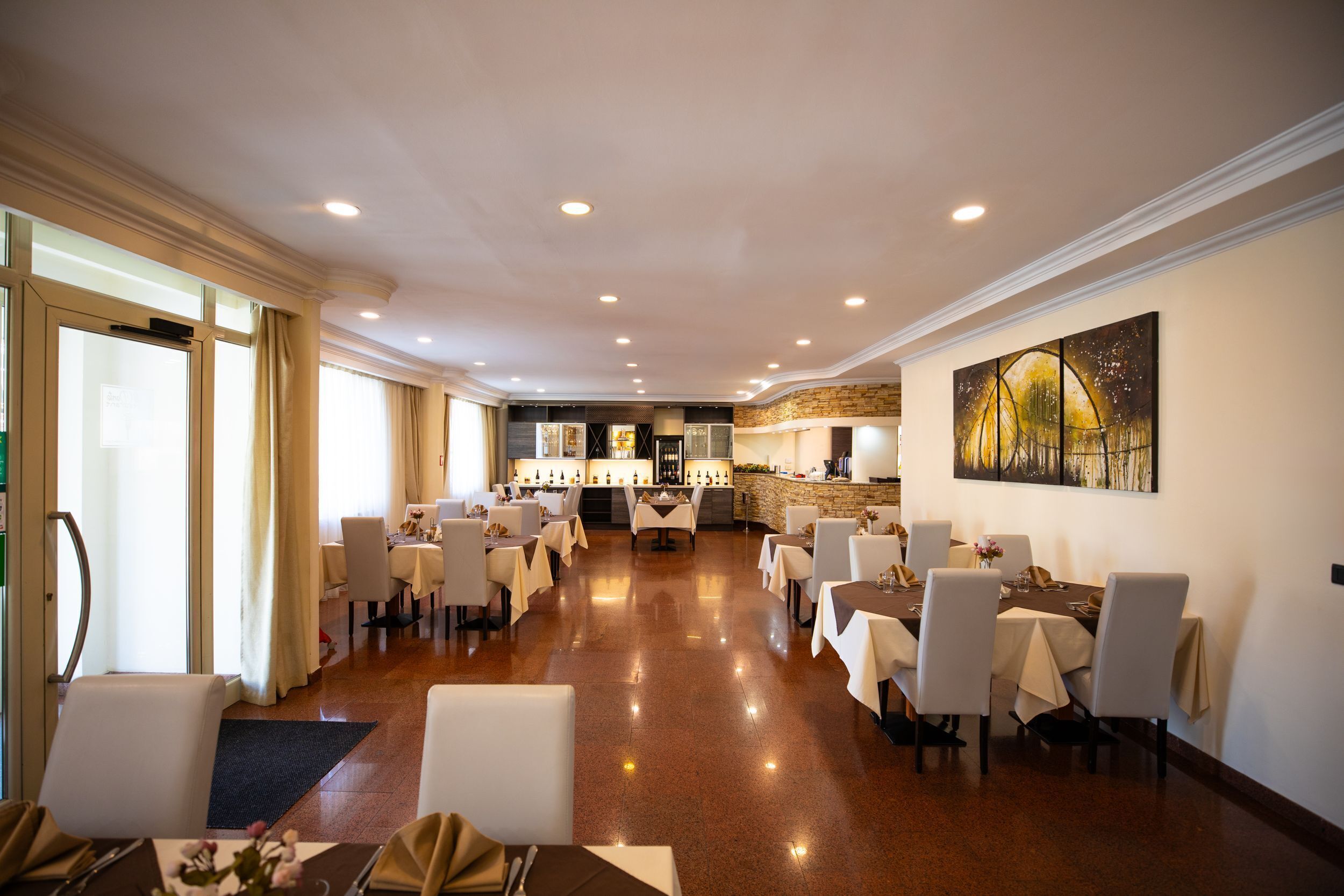 A spacious dining area with multiple tables and chairs, a bar area with a stone accent wall, and a large abstract painting on the wall.