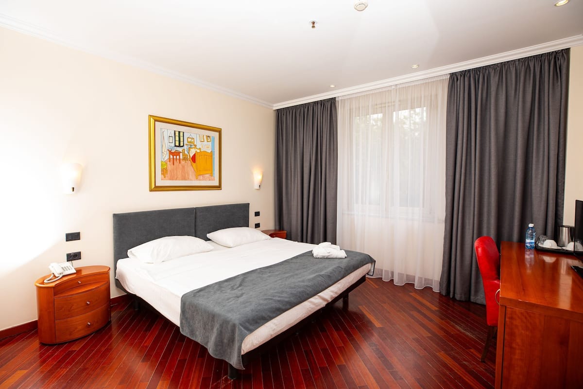 Ein Hotelzimmer mit Bett, Schreibtisch, Stuhl, einem Bild an der Wand und einem Telefon auf dem Nachttisch.