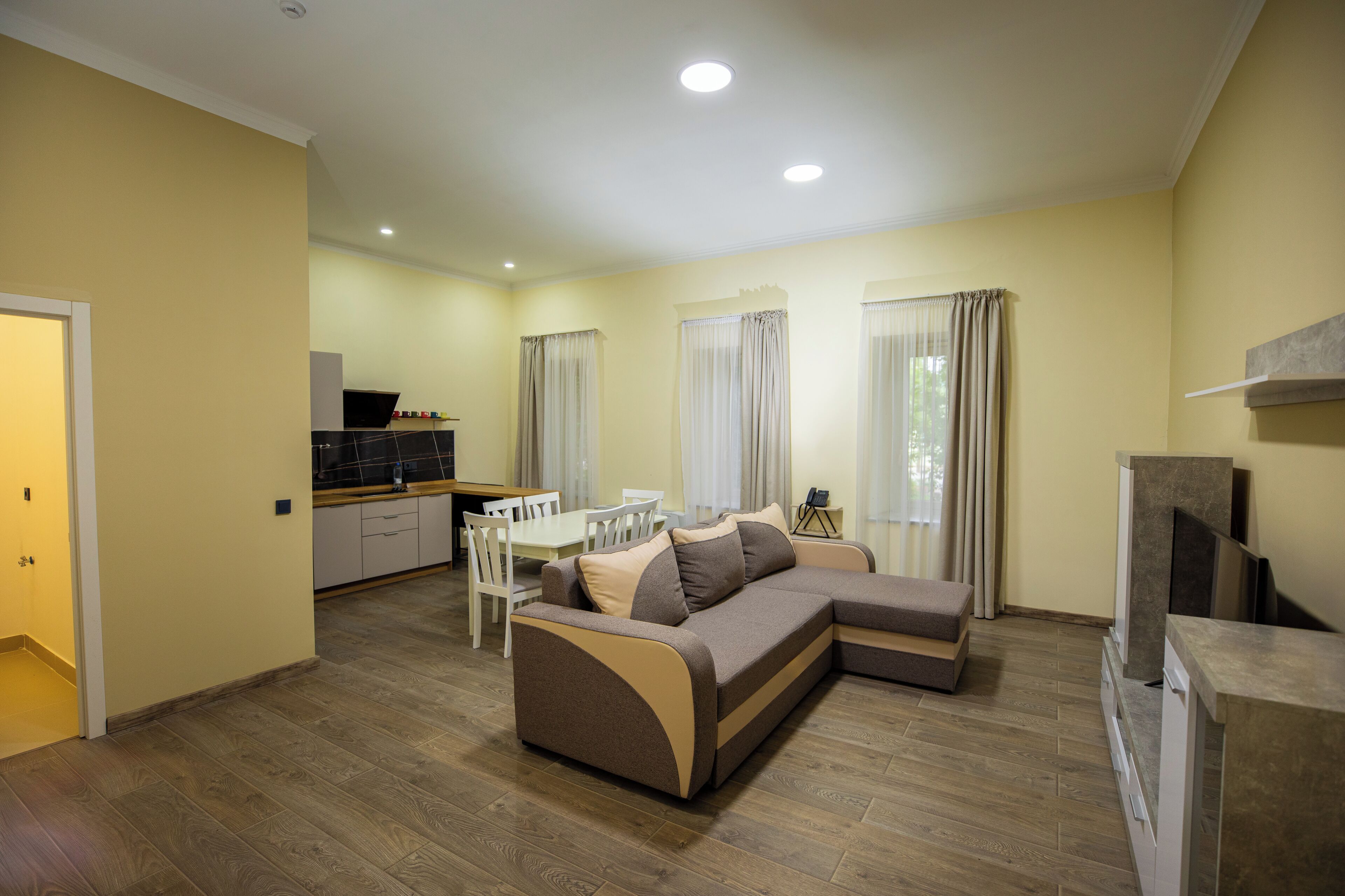 A living room with a sectional sofa, dining table, and chairs, a kitchen area, and a TV.