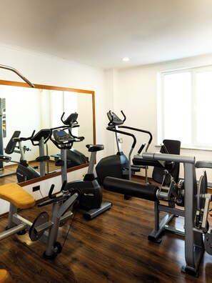 Un gimnasio con equipo de ejercicio, una banca y un espejo.