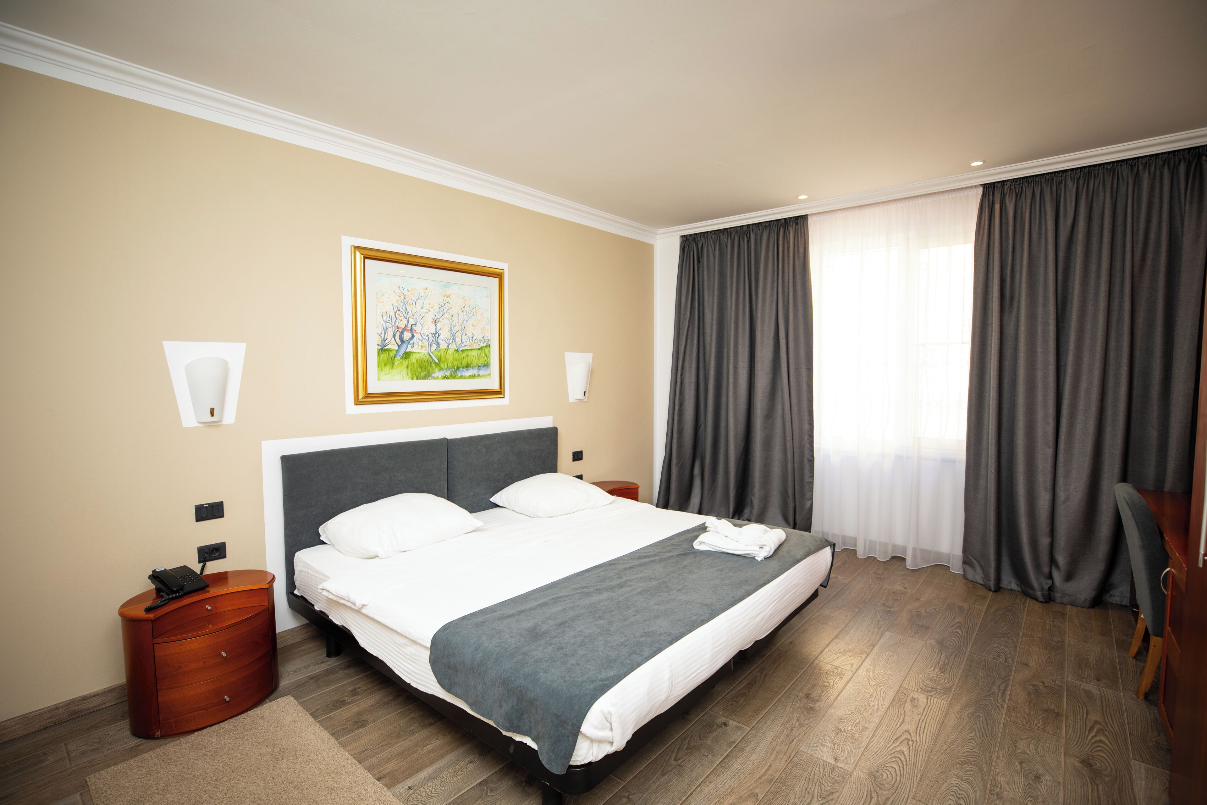 A hotel room with a large bed, a painting on the wall, a telephone, and a nightstand.