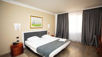 A hotel room with a large bed, a painting on the wall, a telephone, and a nightstand.