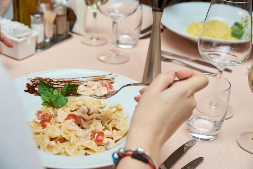 A dining table with a plate of pasta, a glass of water, and a fork.
