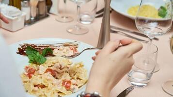 A dining table with a plate of pasta, a glass of water, and a fork.