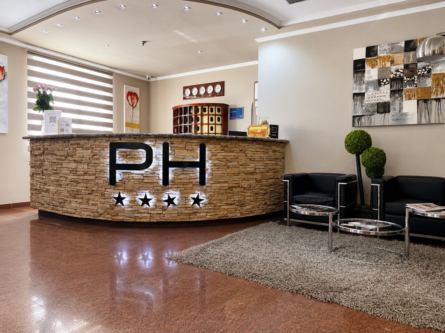 A reception area with a stone counter displaying 'PH' and five stars, a clock, and a wall with a black and white abstract painting.