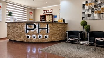 Zona de recepción con mostrador de piedra que muestra 'PH' y cinco estrellas, un reloj y una pared con un cuadro abstracto en blanco y negro.