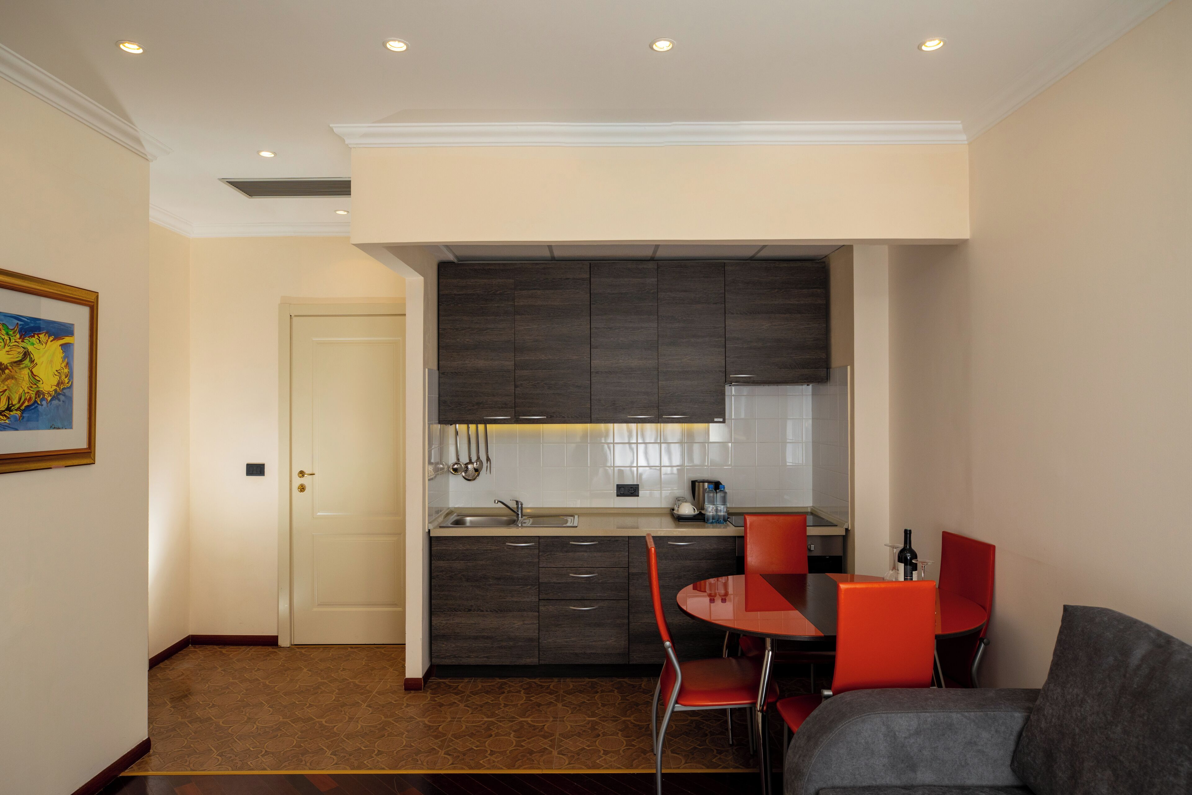 A compact kitchen with dark cabinetry, a sink, and a dining area with red chairs.