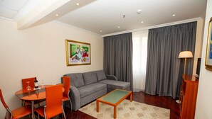 A living room with a gray sofa, orange chairs, a wooden coffee table, and a painting on the wall. - Pushkin Hotel (Uralsk)