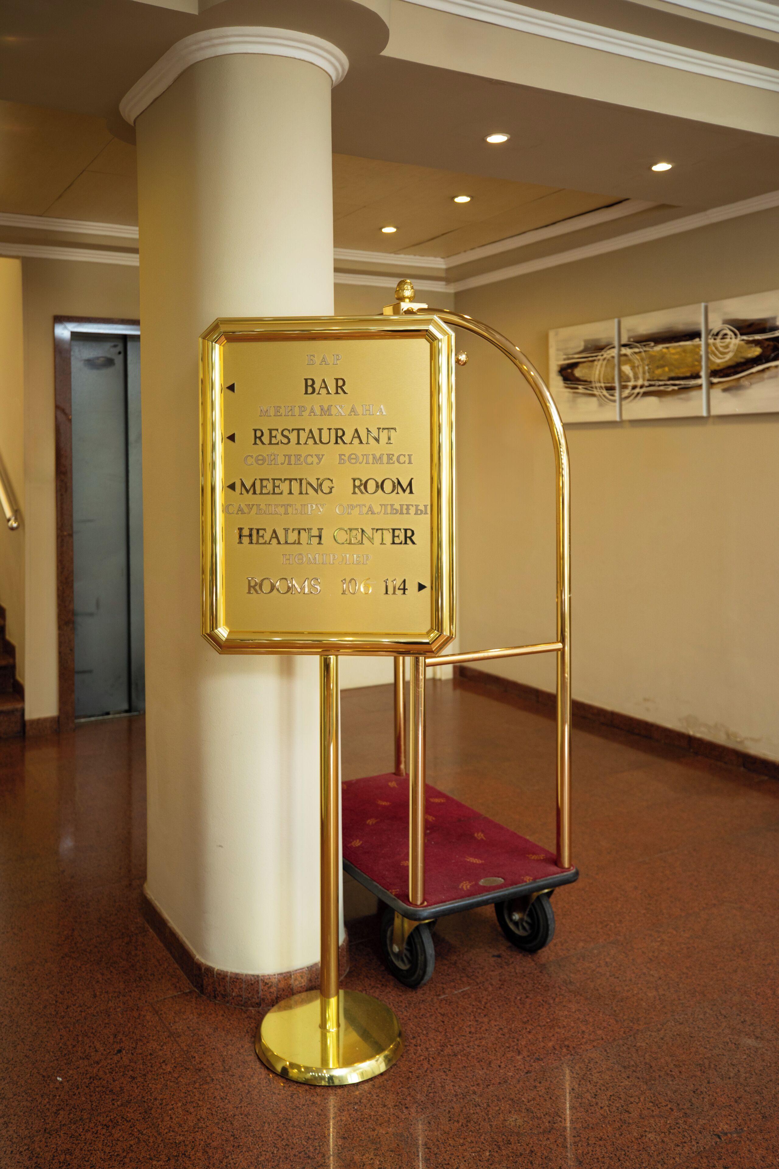 A gold-colored information board with directional arrows and text indicating the locations of a bar, restaurant, meeting room, and health center.