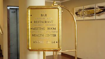 A gold-colored information board with directional arrows and text indicating the locations of a bar, restaurant, meeting room, and health center.