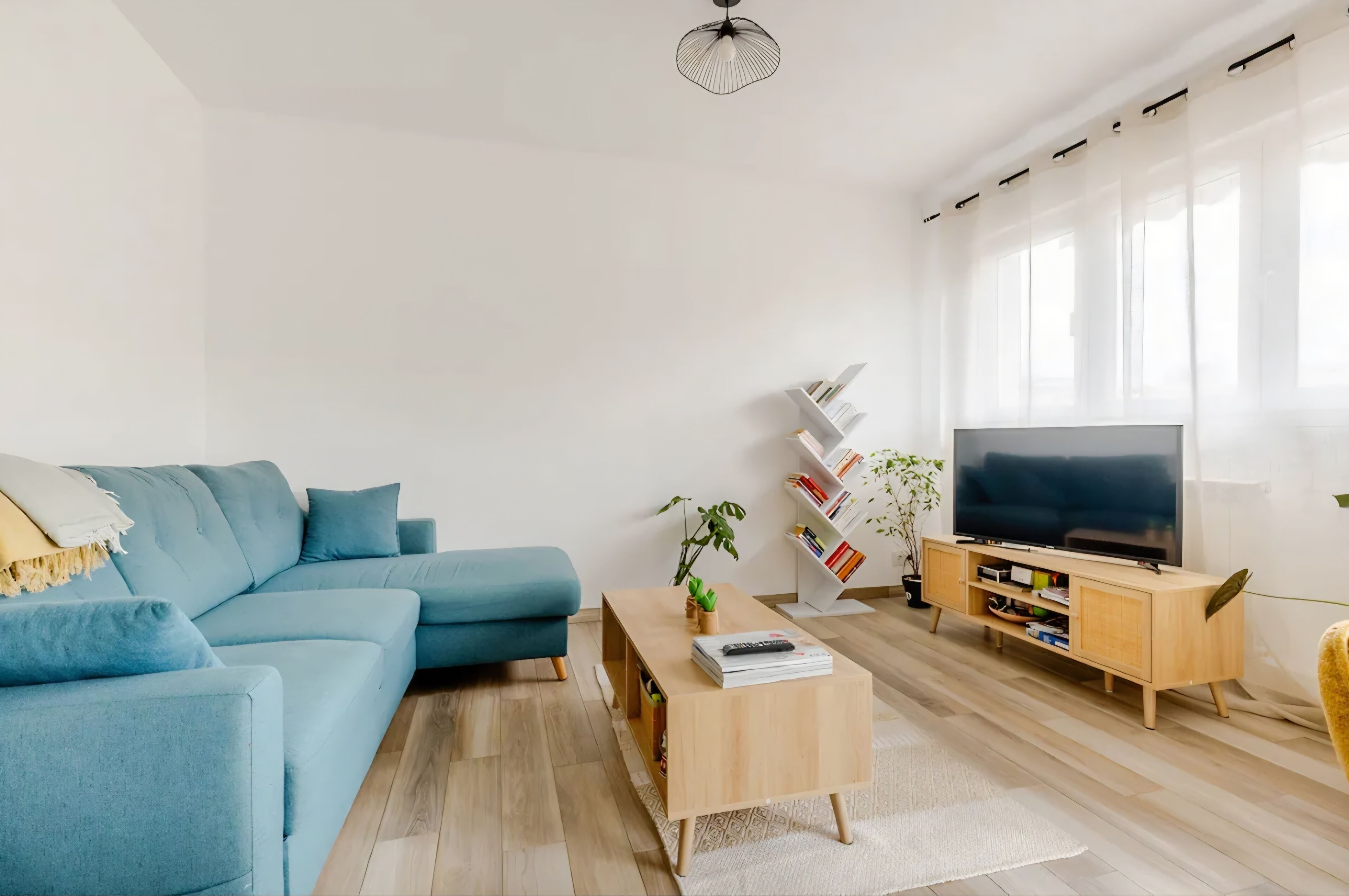 A modern living room with a blue sofa, a wooden coffee table, a TV, and a bookshelf.