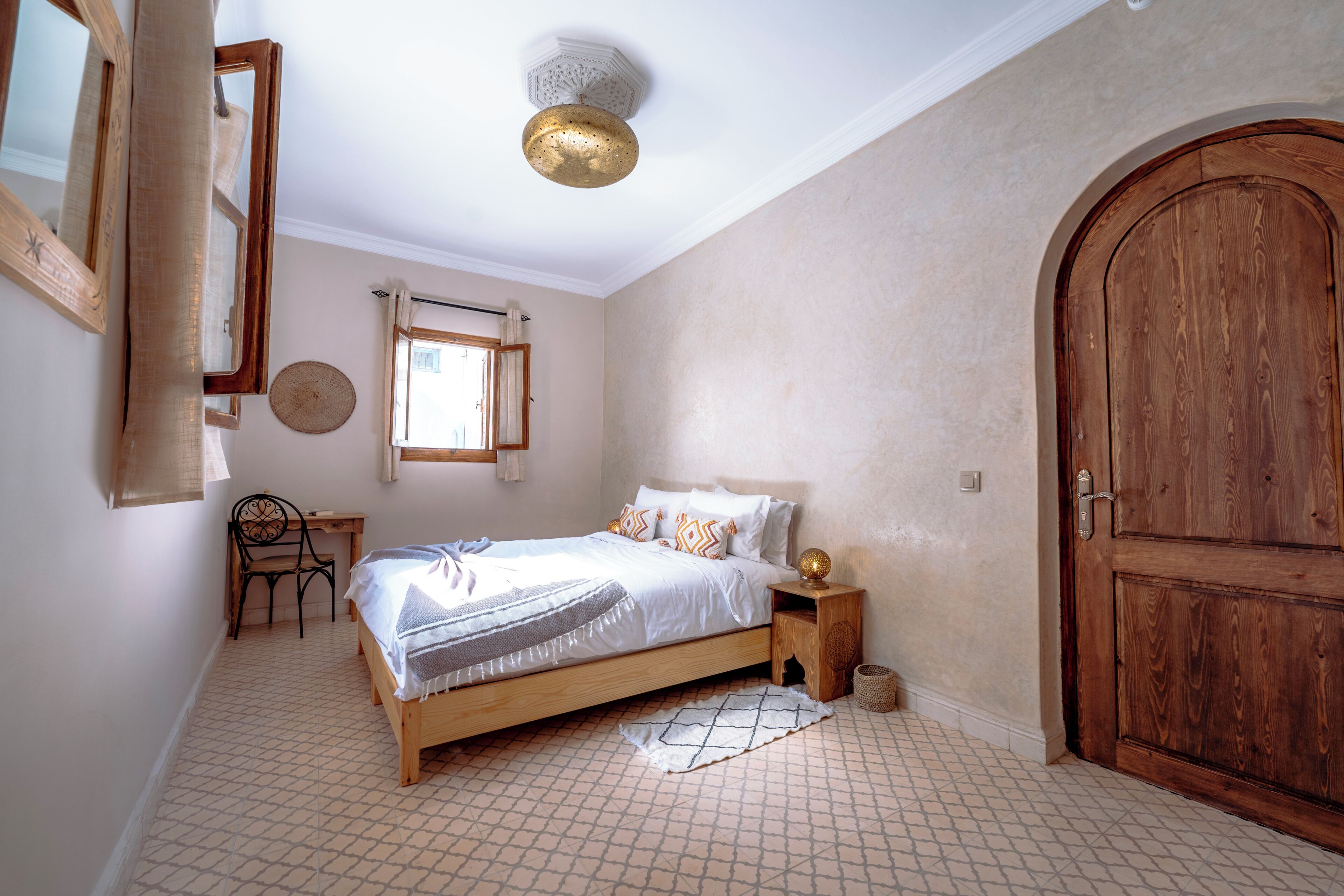 A bedroom with a wooden bed, a round mirror, a desk, and a large wooden door.