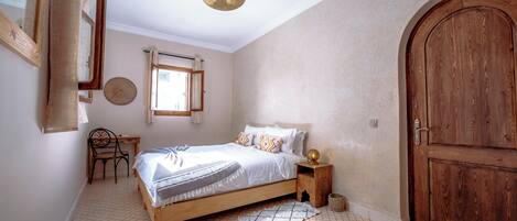 A bedroom with a wooden bed, a round mirror, a desk, and a large wooden door.