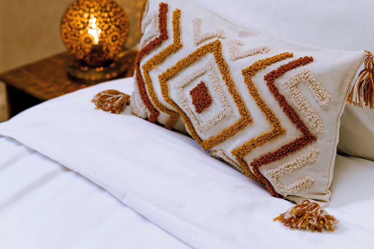 A bed with a white sheet, a decorative pillow with a geometric pattern, and a lit decorative globe on a wooden nightstand.