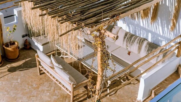 A sunlit outdoor seating area with a pergola, lounge chairs, and a white wall. - Riad Dar Ganne (Essaouira)