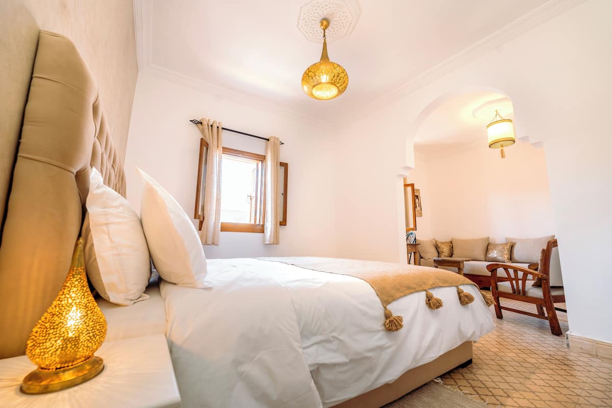 A bedroom with a bed, a lamp, a chair, and a window.