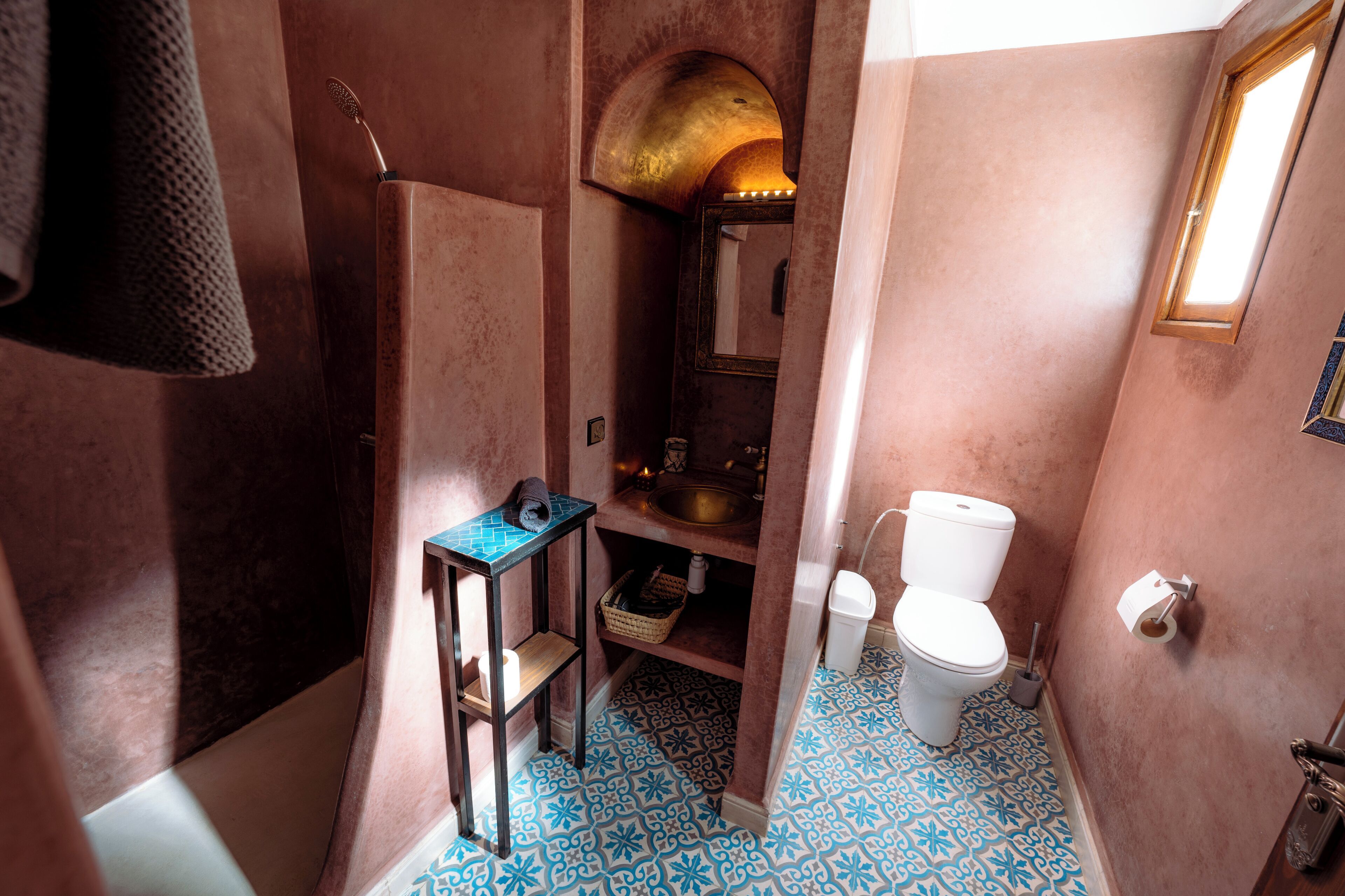 Baño con lavamanos, inodoro y zona de ducha, con baldosas de diseño en el suelo y un perchero.