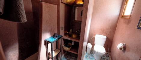 Baño con lavamanos, inodoro y zona de ducha, con baldosas de diseño en el suelo y un perchero.