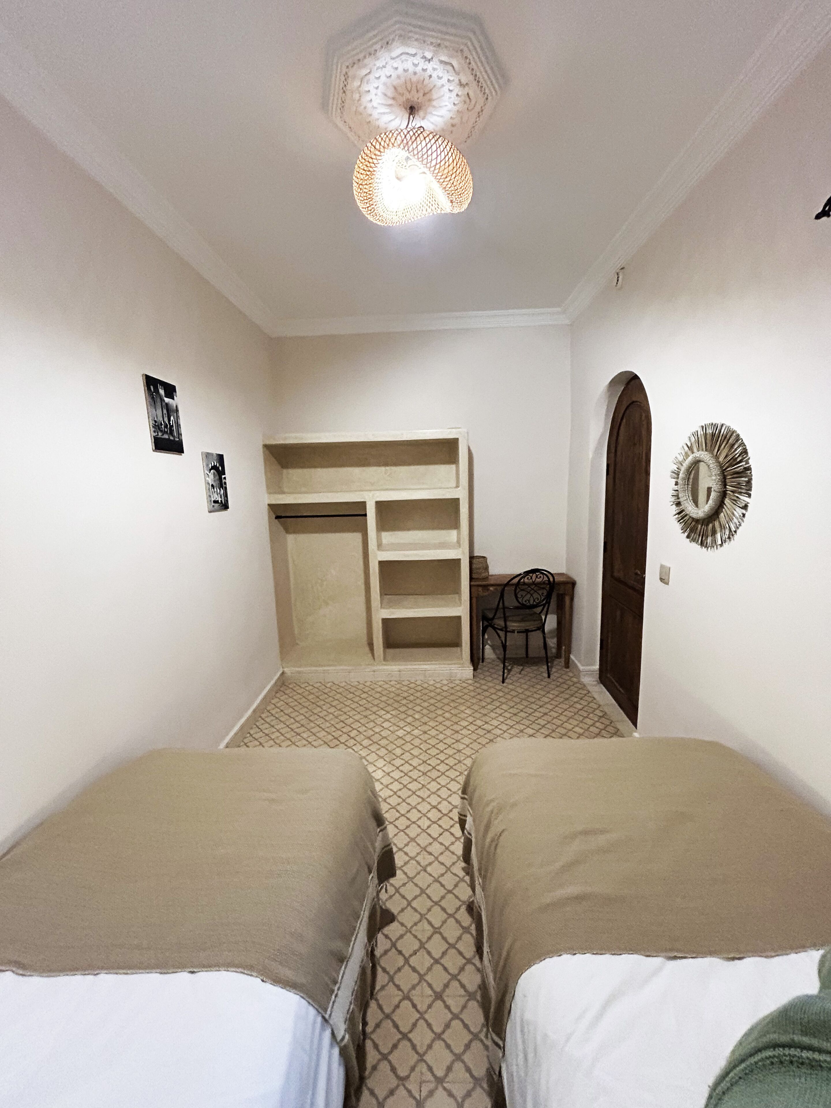 A room with two beds, a desk, a chair, a wardrobe, and a decorative mirror.