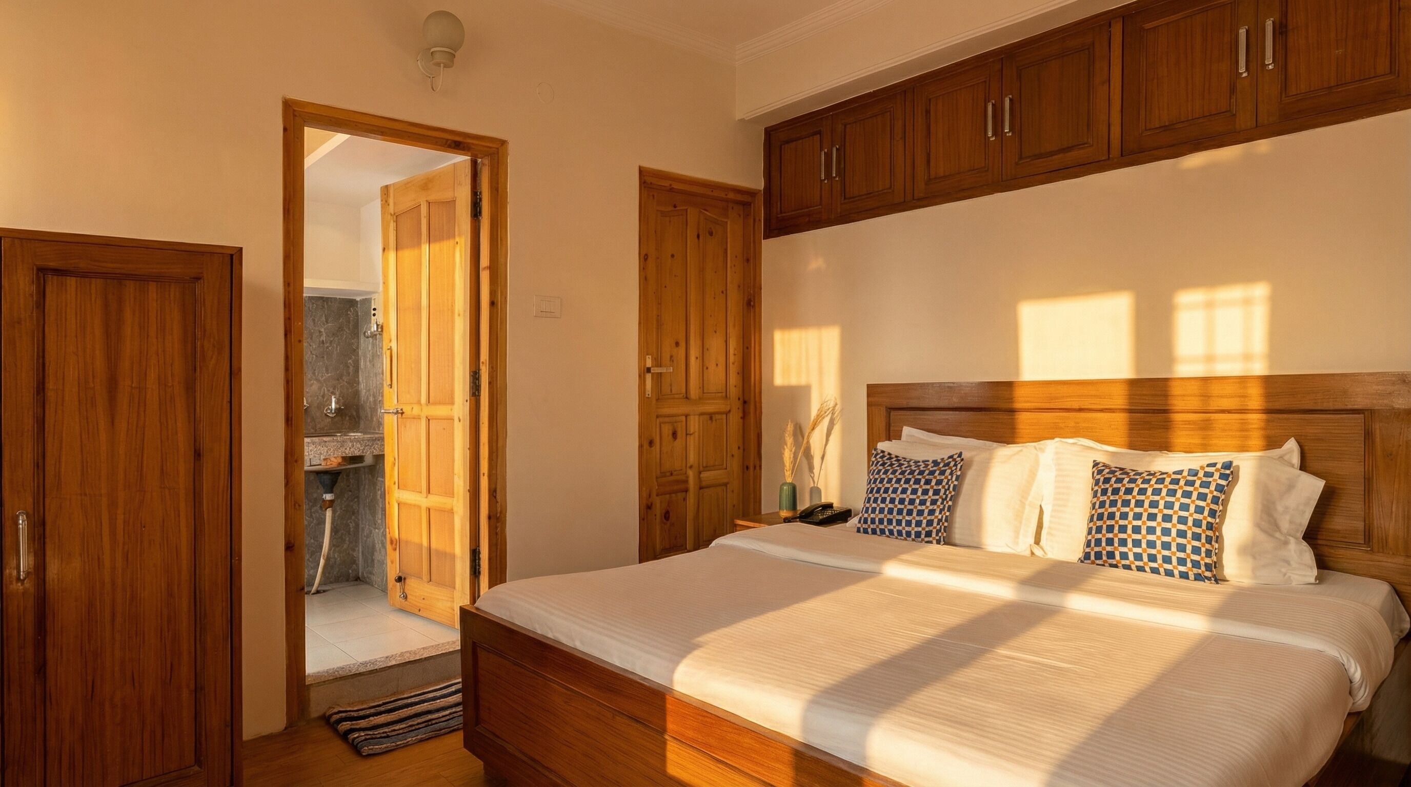 A bedroom with a wooden bed, a wooden wardrobe, and a bathroom visible through an open door.