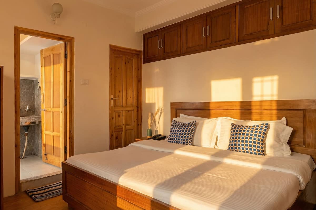 Un dormitorio con cama y armario de madera, y un baño visible a través de una puerta abierta.