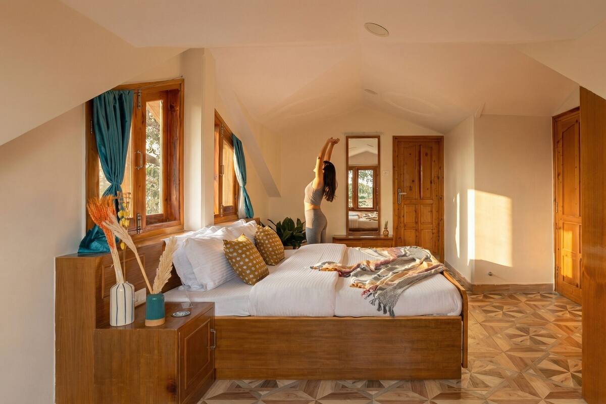 A bedroom with a wooden bed, a nightstand, a mirror, a window with curtains, and a door.