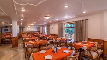 A spacious dining area with multiple tables and chairs, a high ceiling with recessed lighting, and a view of the outdoors through large windows.