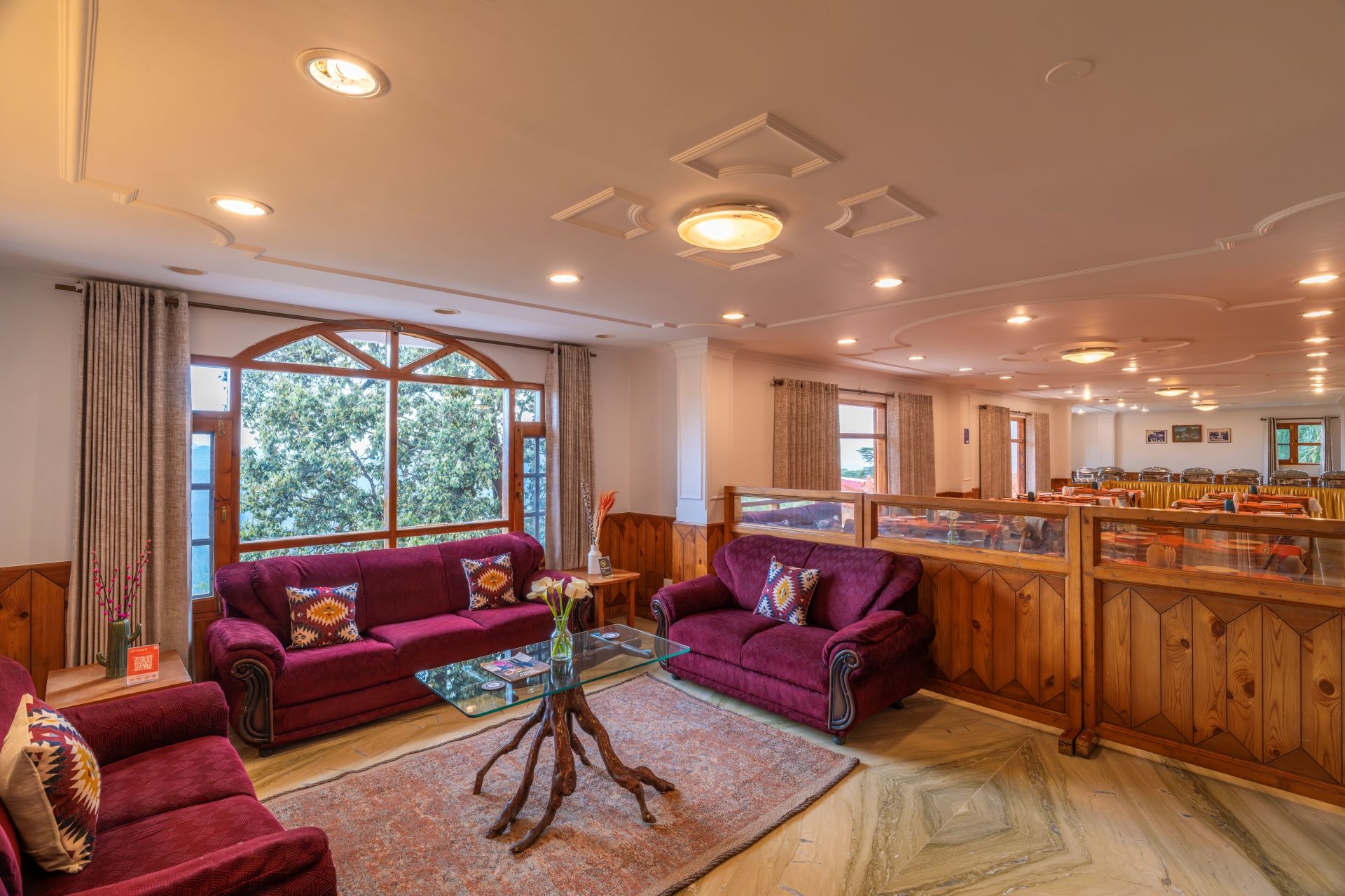 A hotel lobby with two sofas, a glass coffee table, a wooden sideboard, and a view of the outdoors through large windows.