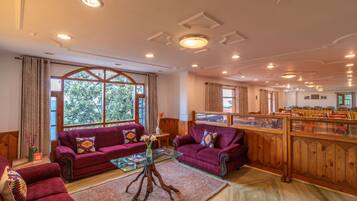 A hotel lobby with two sofas, a glass coffee table, a wooden sideboard, and a view of the outdoors through large windows.