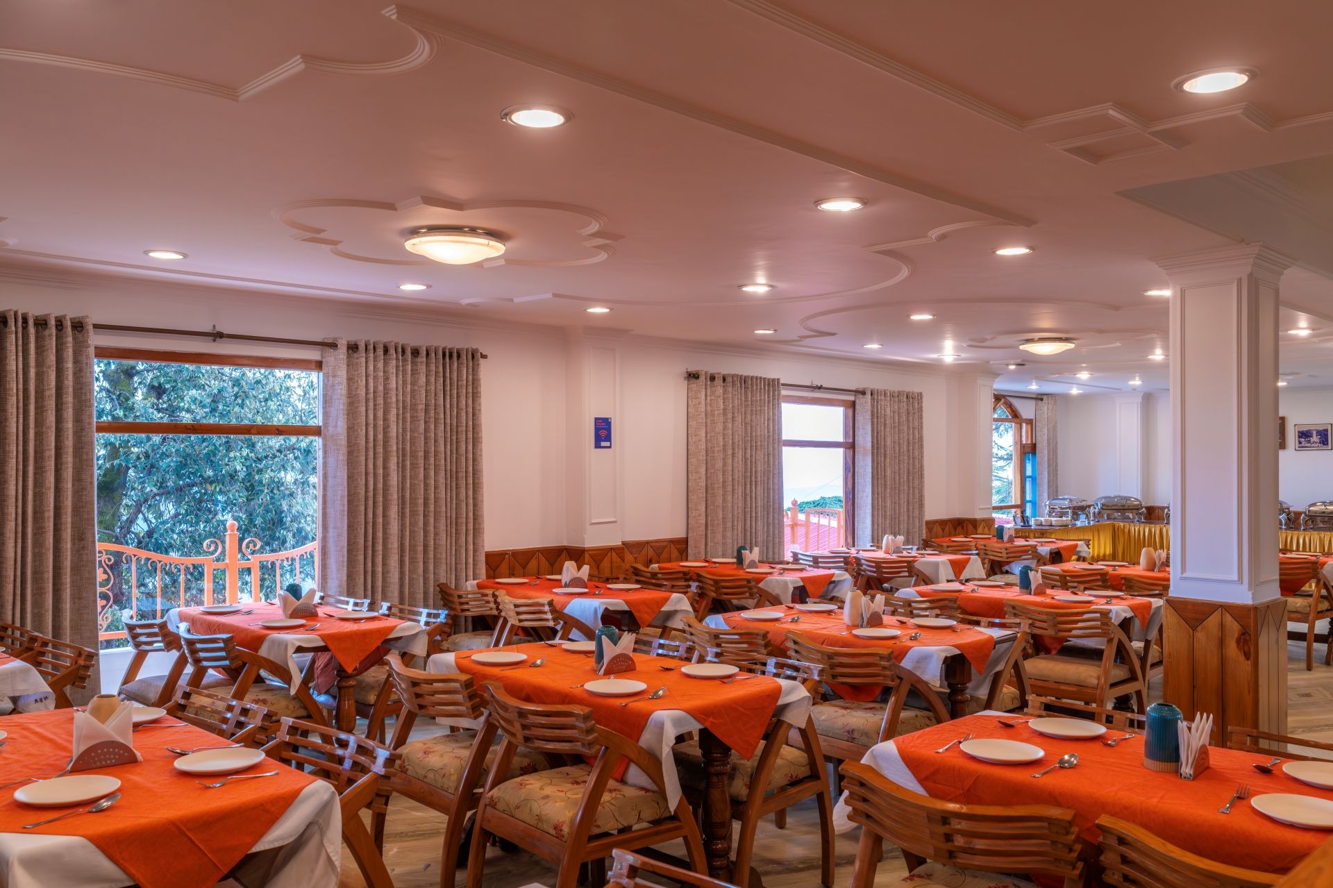 Comedor con varias mesas y sillas, ventanas amplias con cortinas y vistas al exterior.