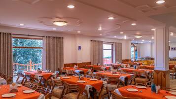 Comedor con varias mesas y sillas, ventanas amplias con cortinas y vistas al exterior.