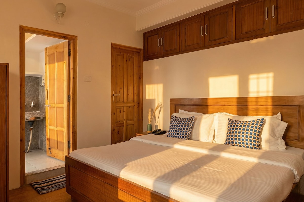 Un dormitorio con cama y armario de madera, y un baño visible a través de una puerta abierta.