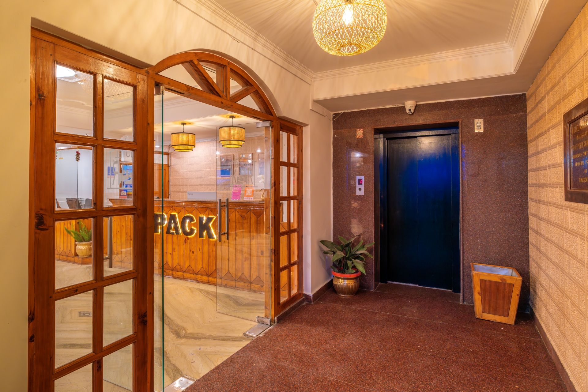 A hotel lobby with a reception desk, a wooden door, a blue elevator, and a potted plant.