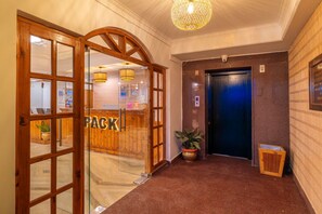 Un vestíbulo de hotel con una recepción, una puerta de madera, un ascensor azul y una planta en maceta.
