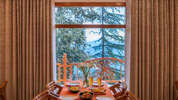 A dining table set with plates, bowls, and glasses, a window with curtains, and a view of trees and mountains.