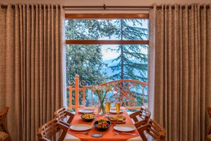 A dining table set with plates, bowls, and glasses, a window with curtains, and a view of trees and mountains.