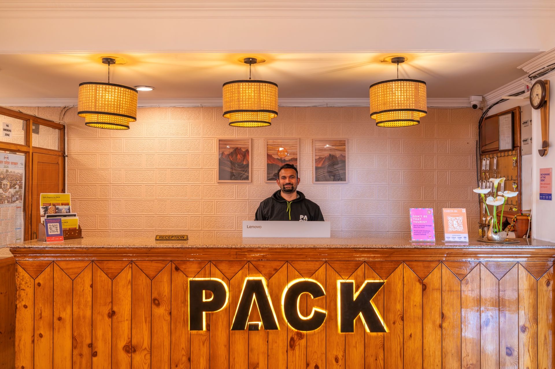 A reception desk with a 'PACK' sign, a man standing behind it, and three hanging lamps.